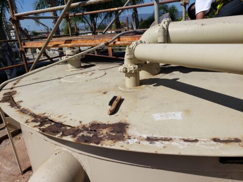 A highly corroded booster tank of a wastewater facility is displayed alongside a wire brush ready to be cleaned for repair